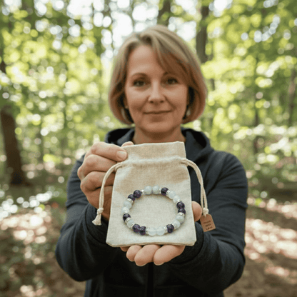 Una mujer en un bosque soleado ofrece una Pulsera Serena - Alivio Natural para la Menopausia, mostrando sus piedras blancas y moradas para la menopausia de una bolsa con cordón y sonriendo amablemente mientras comparte alivio síntomas menopausia.